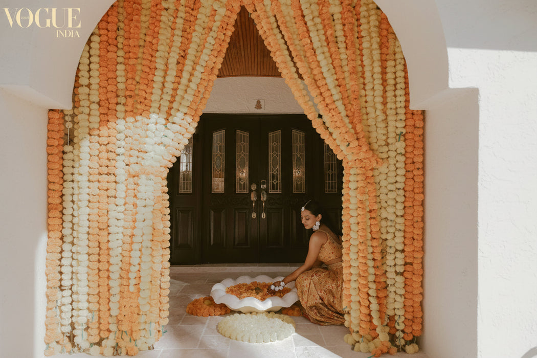 Woman sitting on a decorative platform with orange and white floral arrangements in the foreground.