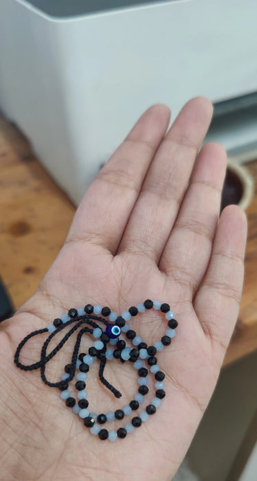 Hand holding a small black and blue beaded necklace on a wooden surface.
