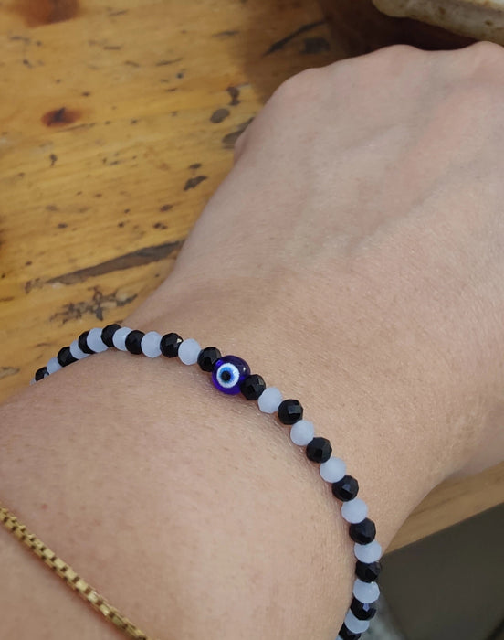 Hand wearing a black and white beaded bracelet with an evil eye charm 