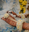 Close-up of hands with henna designs and floral decorations, wearing a blue and white patterned dress.
