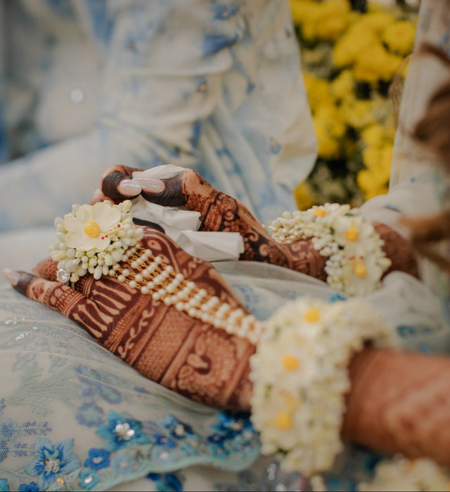 Close-up of hands with henna designs and floral decorations, wearing a blue and white patterned dress.