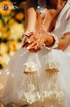 A close-up image of a bridal bangle with attached floral kaleere, featuring a intricate design with silk flowers and beads, held by a hand with nail art.