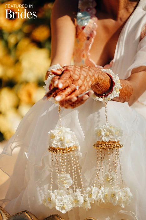 A close-up image of a bridal bangle with attached floral kaleere, featuring a intricate design with silk flowers and beads, held by a hand with nail art.