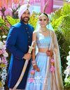 Man in traditional blue outfit and woman in light blue and gold traditional attire with 'Prune India' branding.