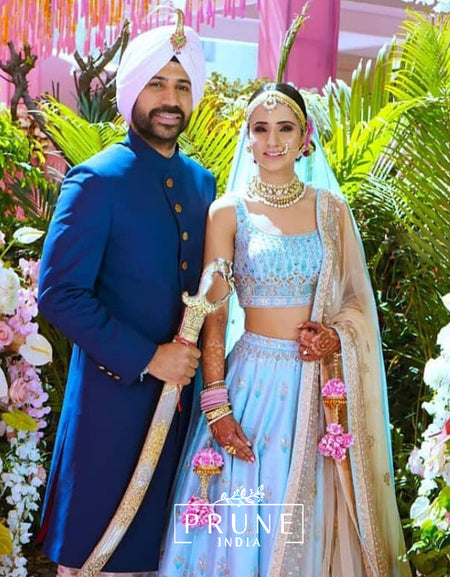 Man in traditional blue outfit and woman in light blue and gold traditional attire with 'Prune India' branding.