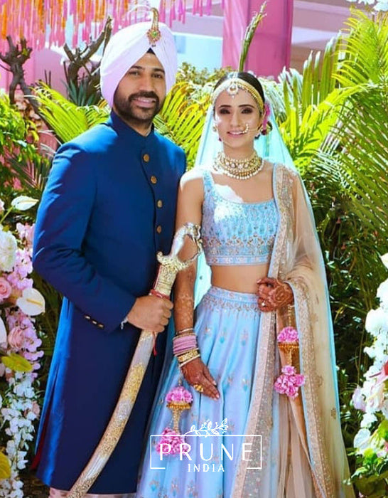 Man in traditional blue outfit and woman in light blue and gold traditional attire with 'Prune India' branding.