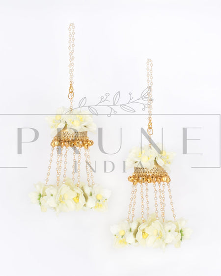 A pair of traditional Indian bridal earrings, featuring gold-colored metalwork and white floral designs, hanging against a plain background.